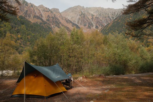 Serene autumn camping scene in Kamikochi, Matsumoto, with a vibrant tent and majestic mountain backdrop.