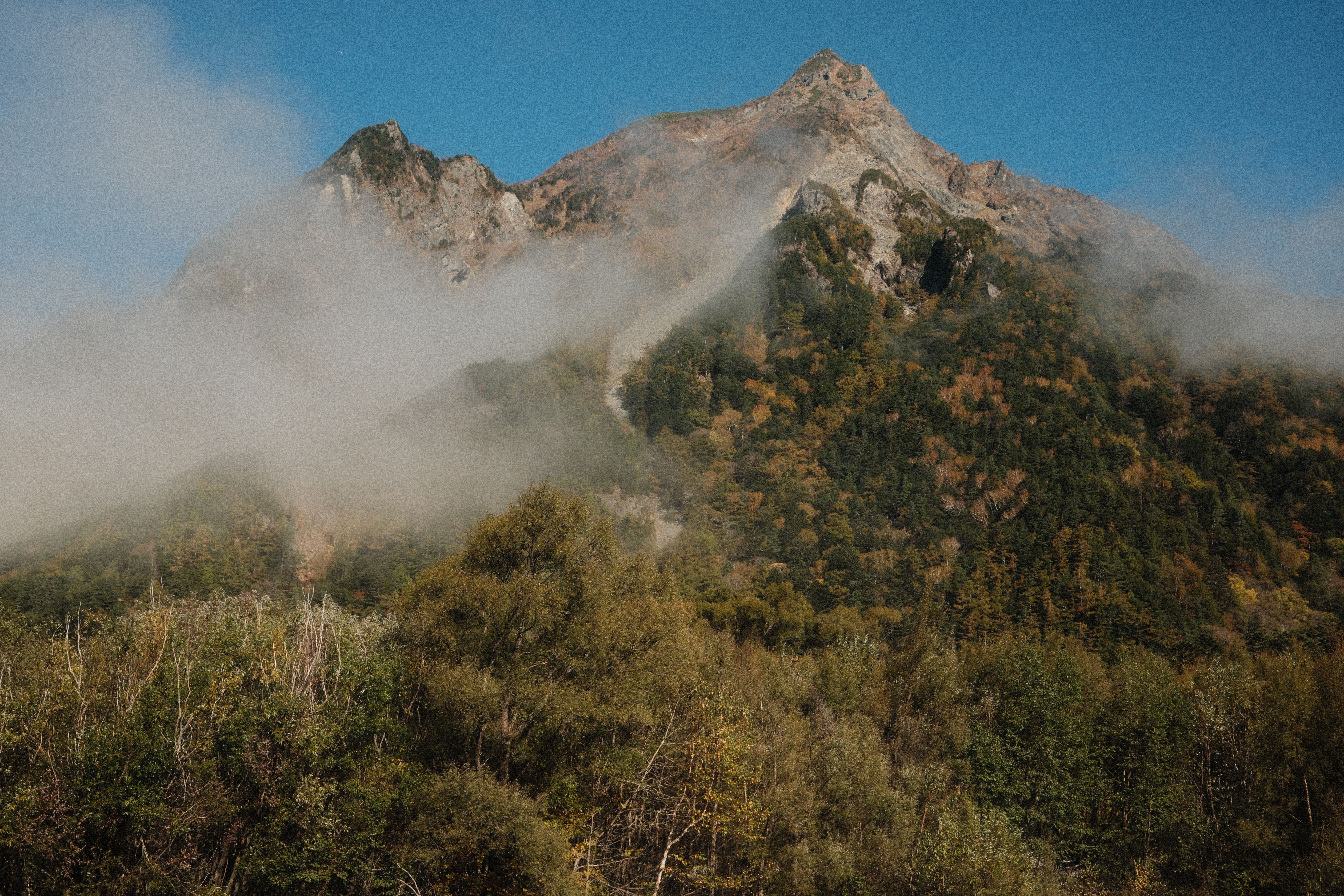 Fog drapes over the lush slopes of Mount Yake in Matsumoto, Nagano, Japan, during a crisp autumn day.