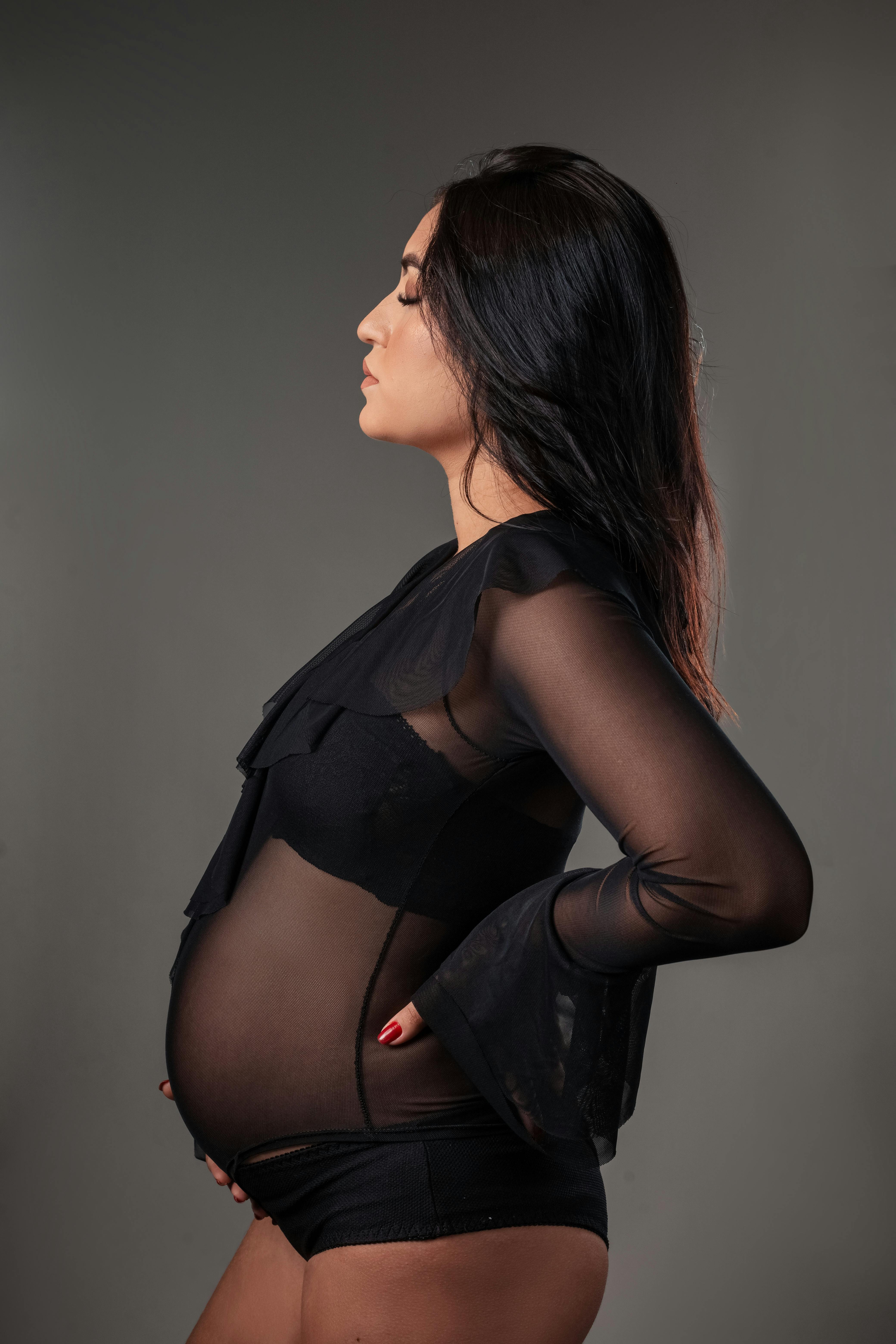Side profile portrait of a pregnant woman in a sheer black outfit, highlighting growth and maternity.