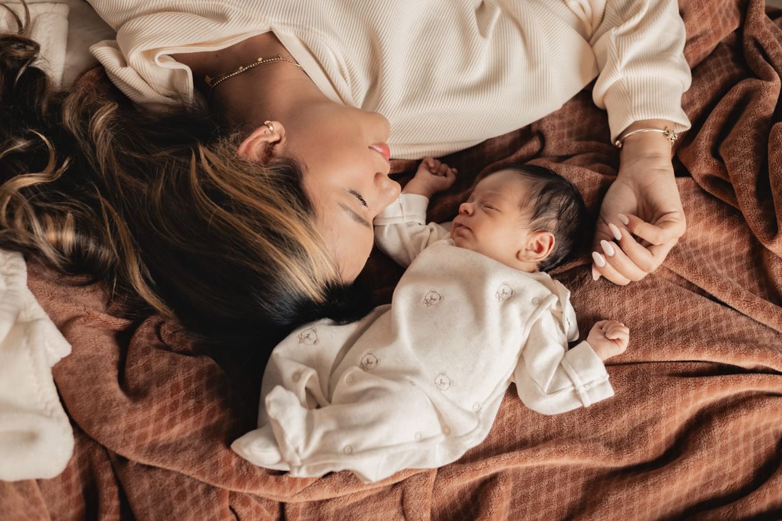 Mother resting beside her peacefully sleeping newborn baby