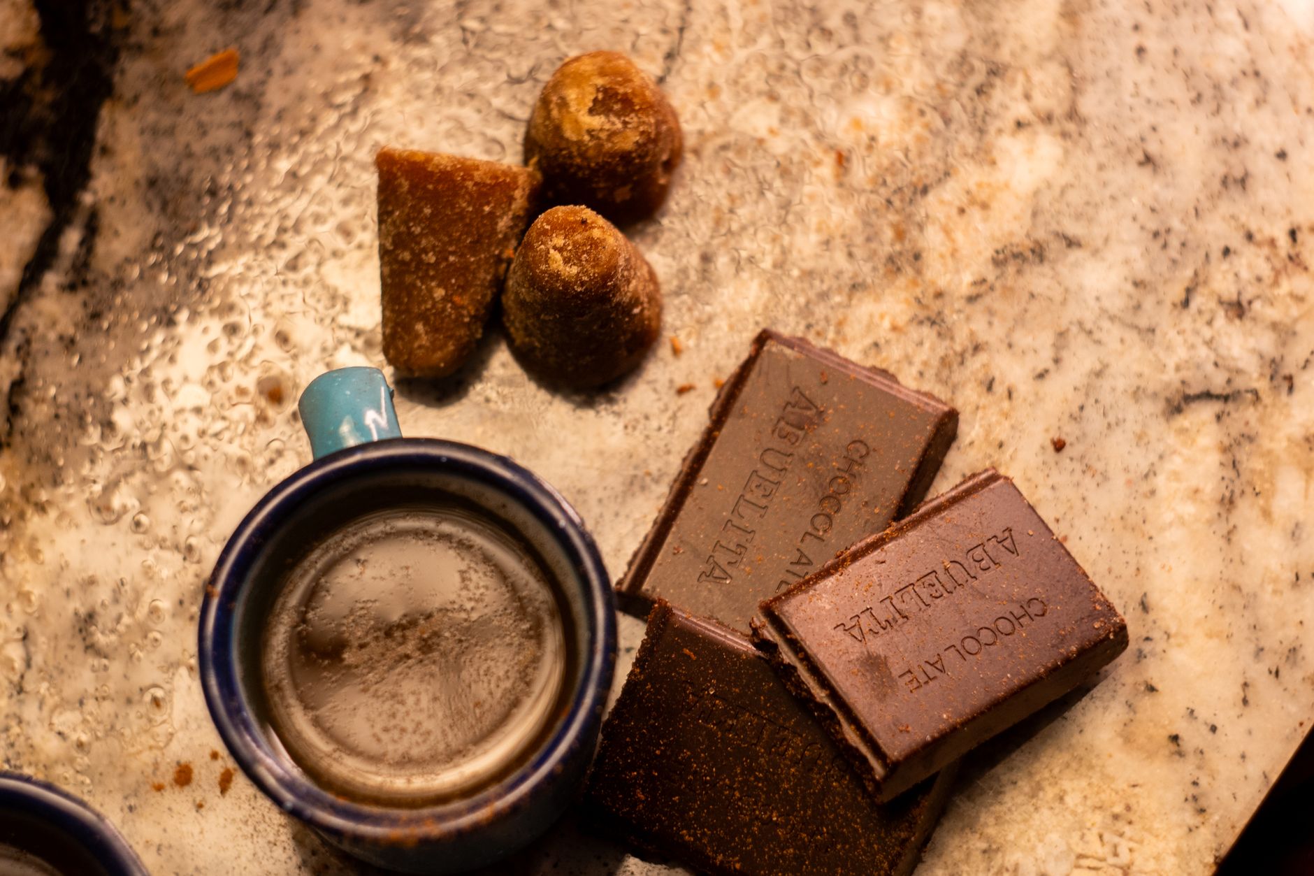 A traditional Mexican cup of café de olla with chocolate and piloncillo on a rustic surface.