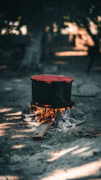A large black pot heats over an open fire outdoors, creating a rustic cooking scene.