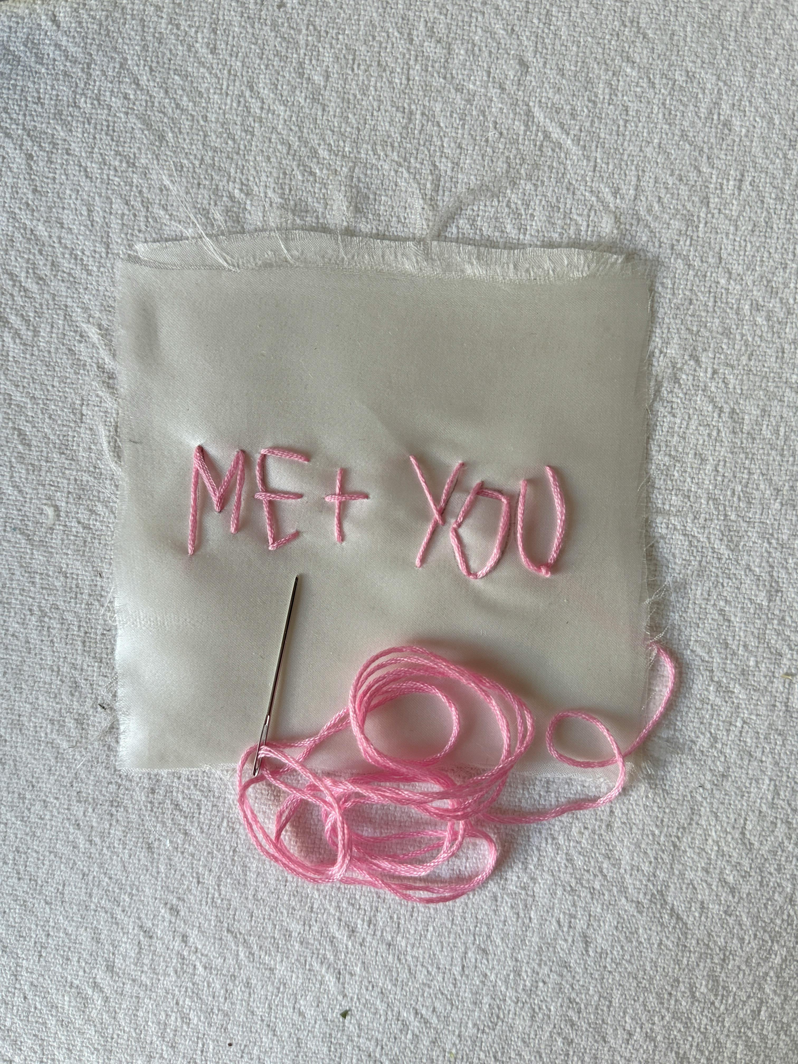 Pink thread embroidery on white fabric with 'Me + You.'