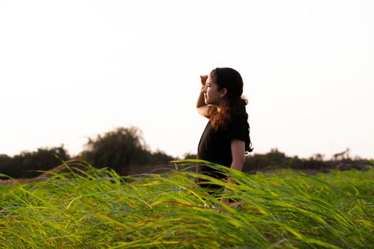 Young girl in a green field looking into the distance under a clear sky, enjoying nature.