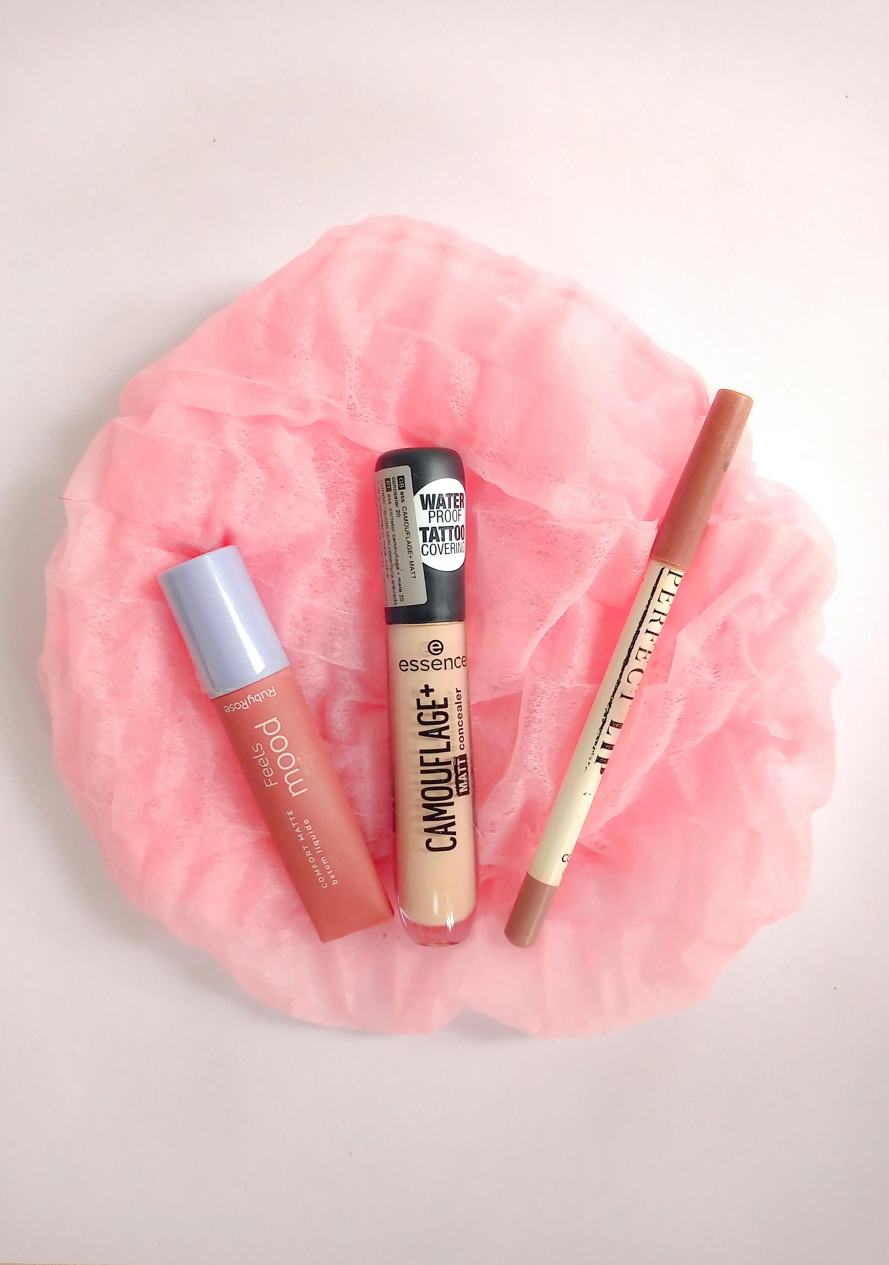 A minimalist flat lay of various makeup products on a pink fabric background.
