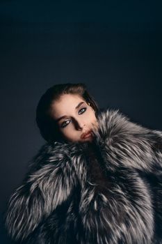 Stylish portrait of a woman in a plush fur coat with dramatic lighting.