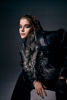 Stylish woman posing in a black leather outfit with fur detail, confident and chic look.