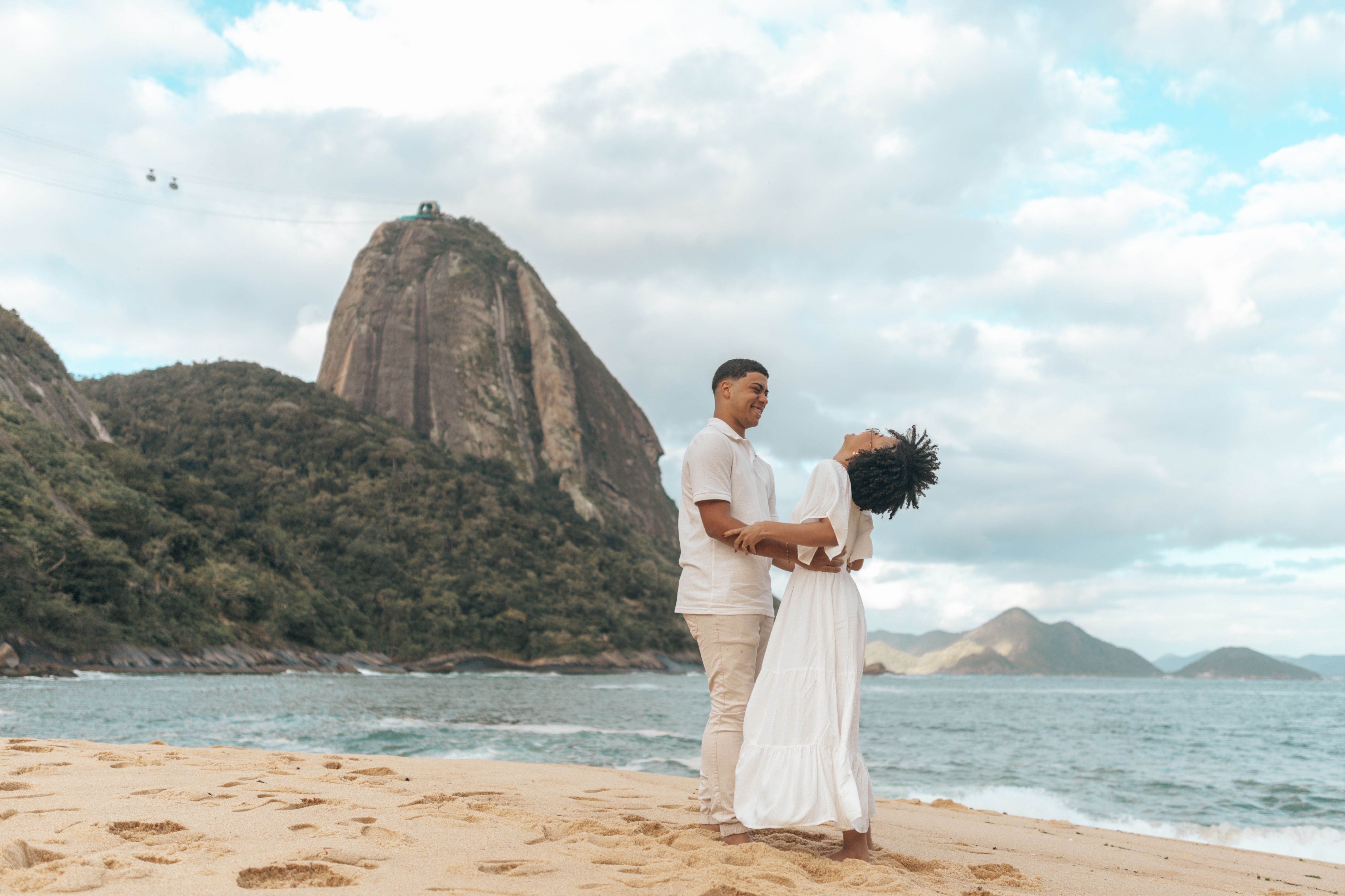 Casal apaixonado em praia paradisíaca com Pão de Açúcar ao fundo, ideal para lua de mel de luxo.
