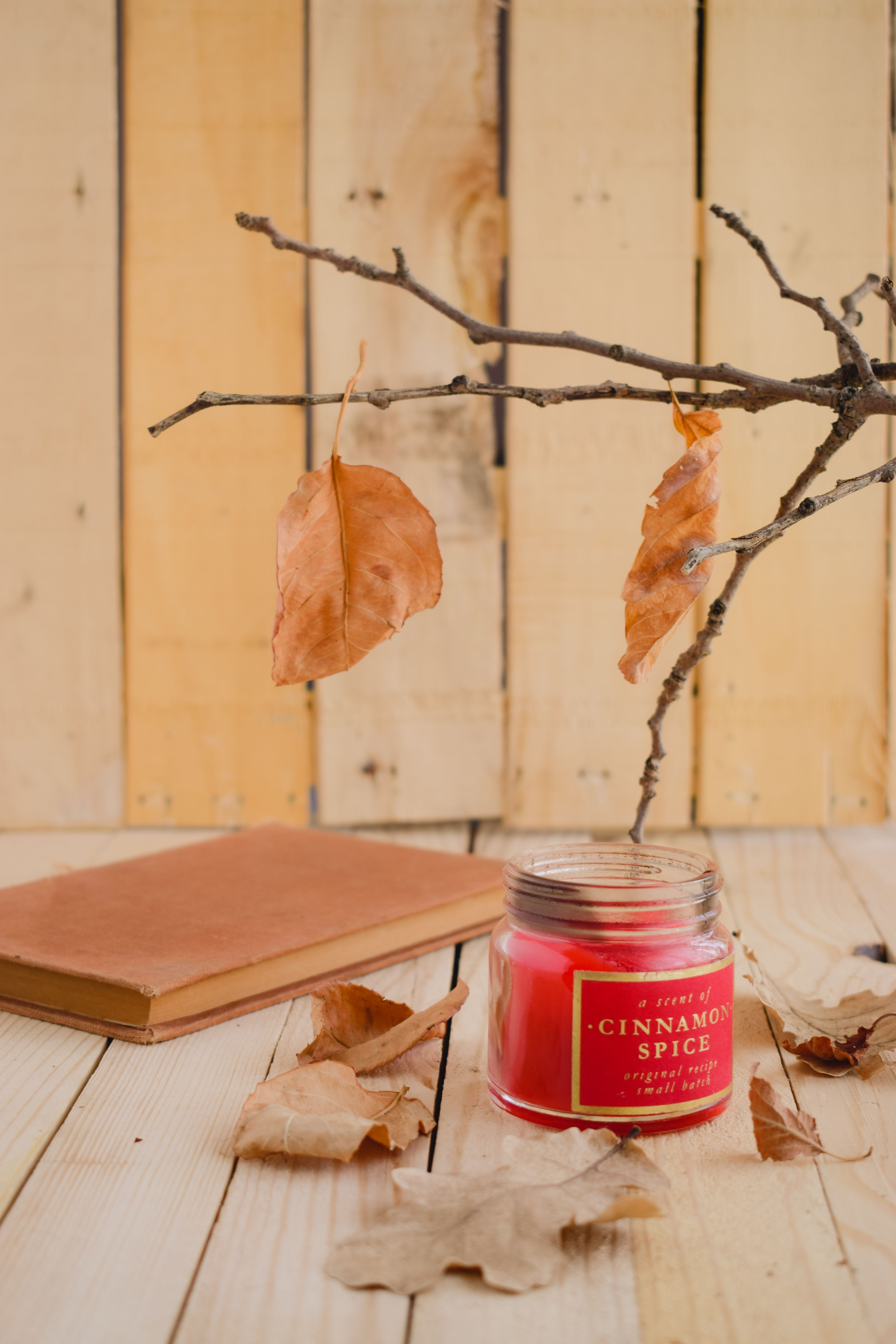 Warm autumn scene with cinnamon spice scented candle and leaves indoors.