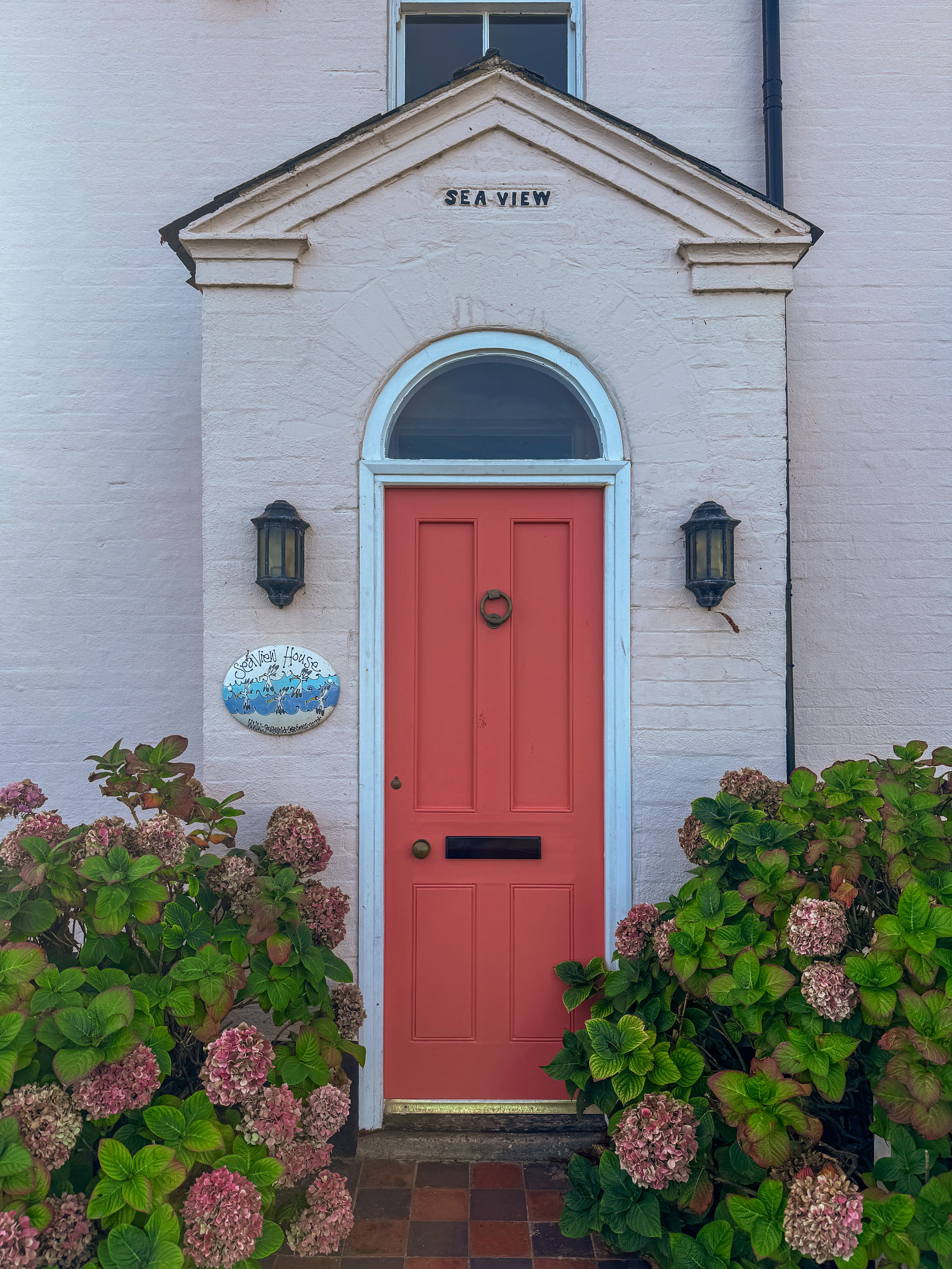 A picturesque English doorway with an orange door, surrounded by hydrangeas in Southwold, UK.