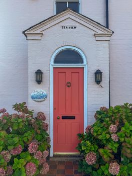 A picturesque English doorway with an orange door, surrounded by hydrangeas in Southwold, UK.