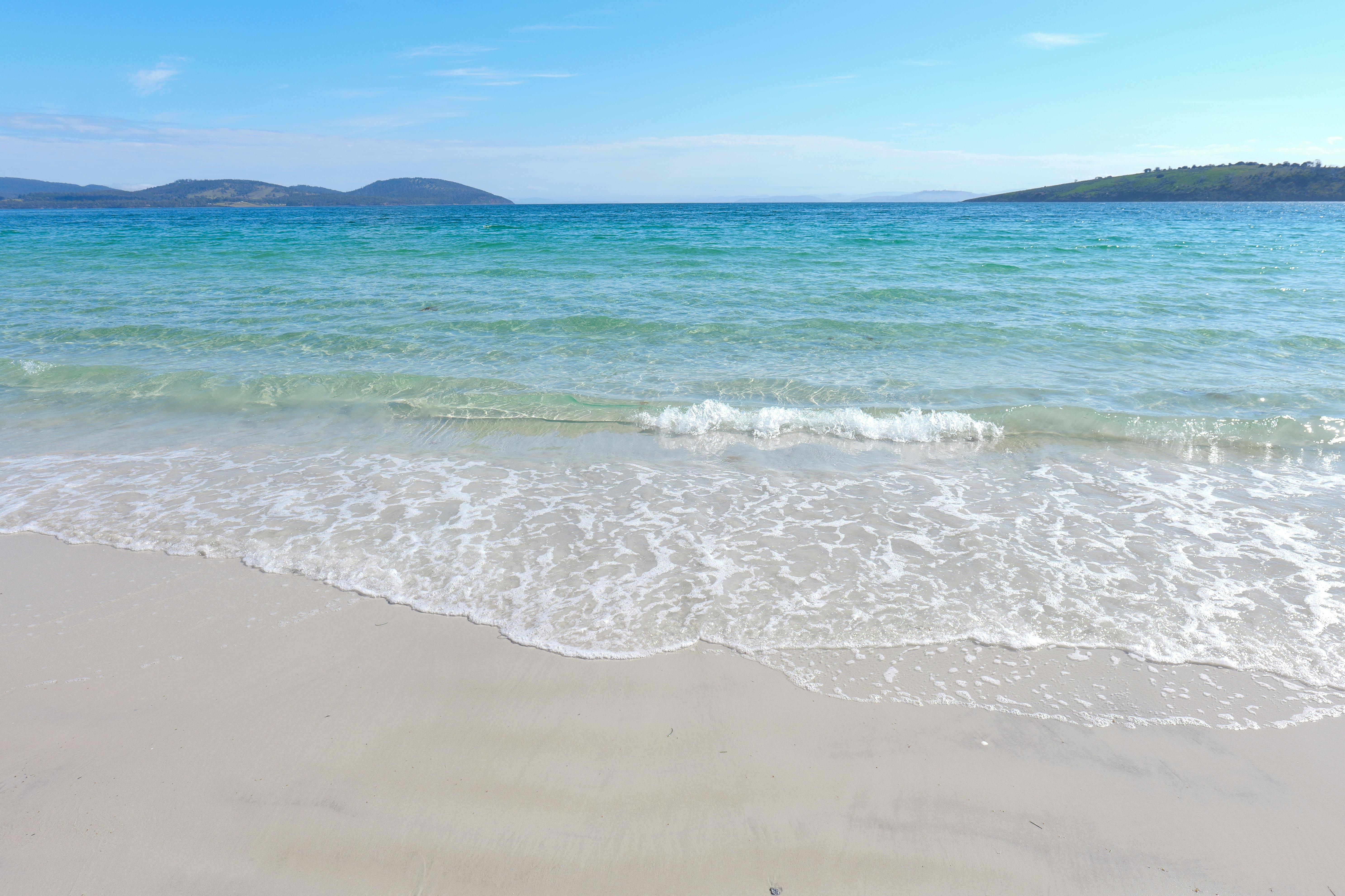 Crystal clear ocean waves on a sandy beach in Tasmania, Australia.