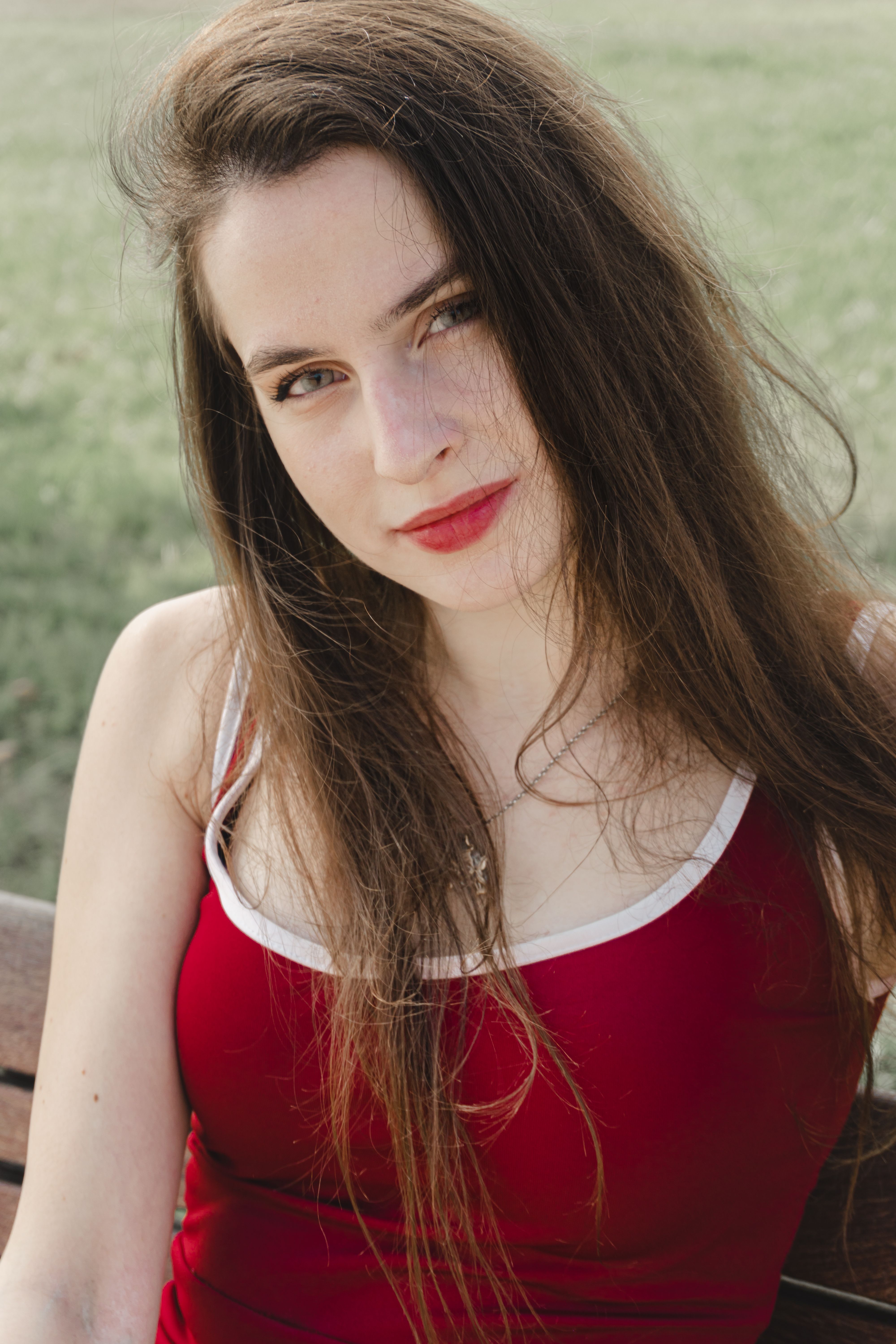 Portrait of a young woman with long hair wearing a red dress sitting outdoors.