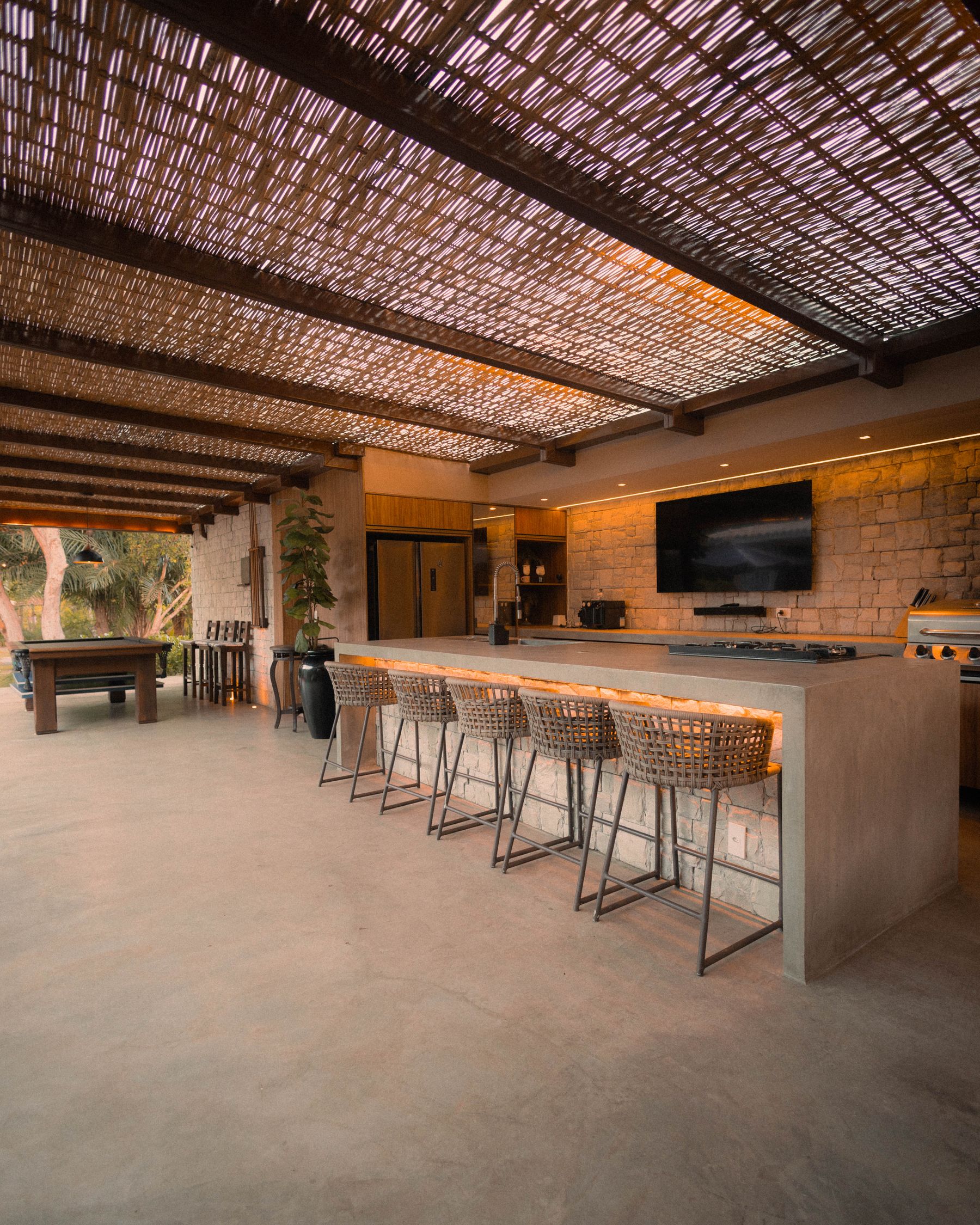 Spacious covered outdoor kitchen with bar, seating and warm architectural finishes