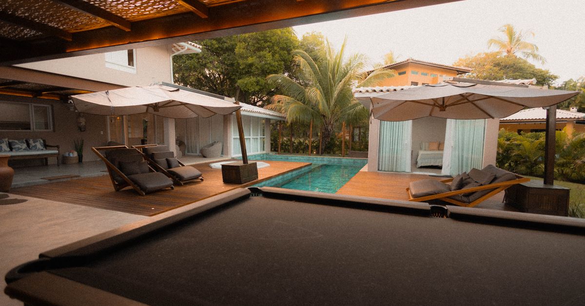 Cozy tropical outdoor area featuring a modern pool, lounge chairs, and exotic greenery under a warm sunset.