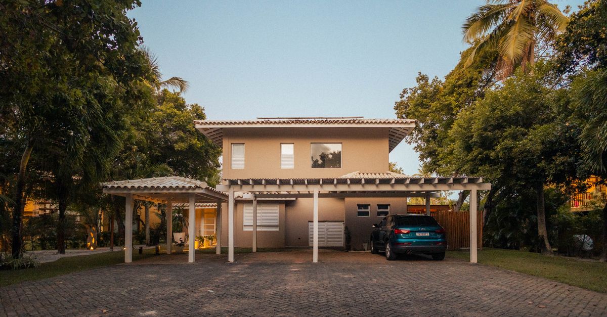 Exterior view of a modern house with a driveway and palm trees at sunset, offering a serene tropical ambiance.