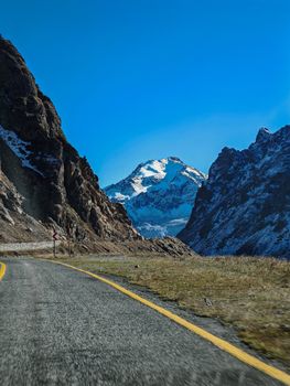 A beautiful mountain road with snow-capped peak under clear blue sky, perfect for travel inspiration.