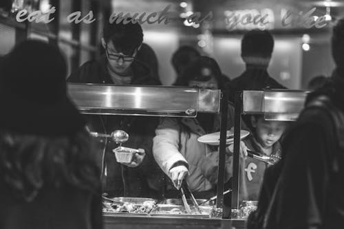 Grayscale Photo of Children Taking Food from Counter