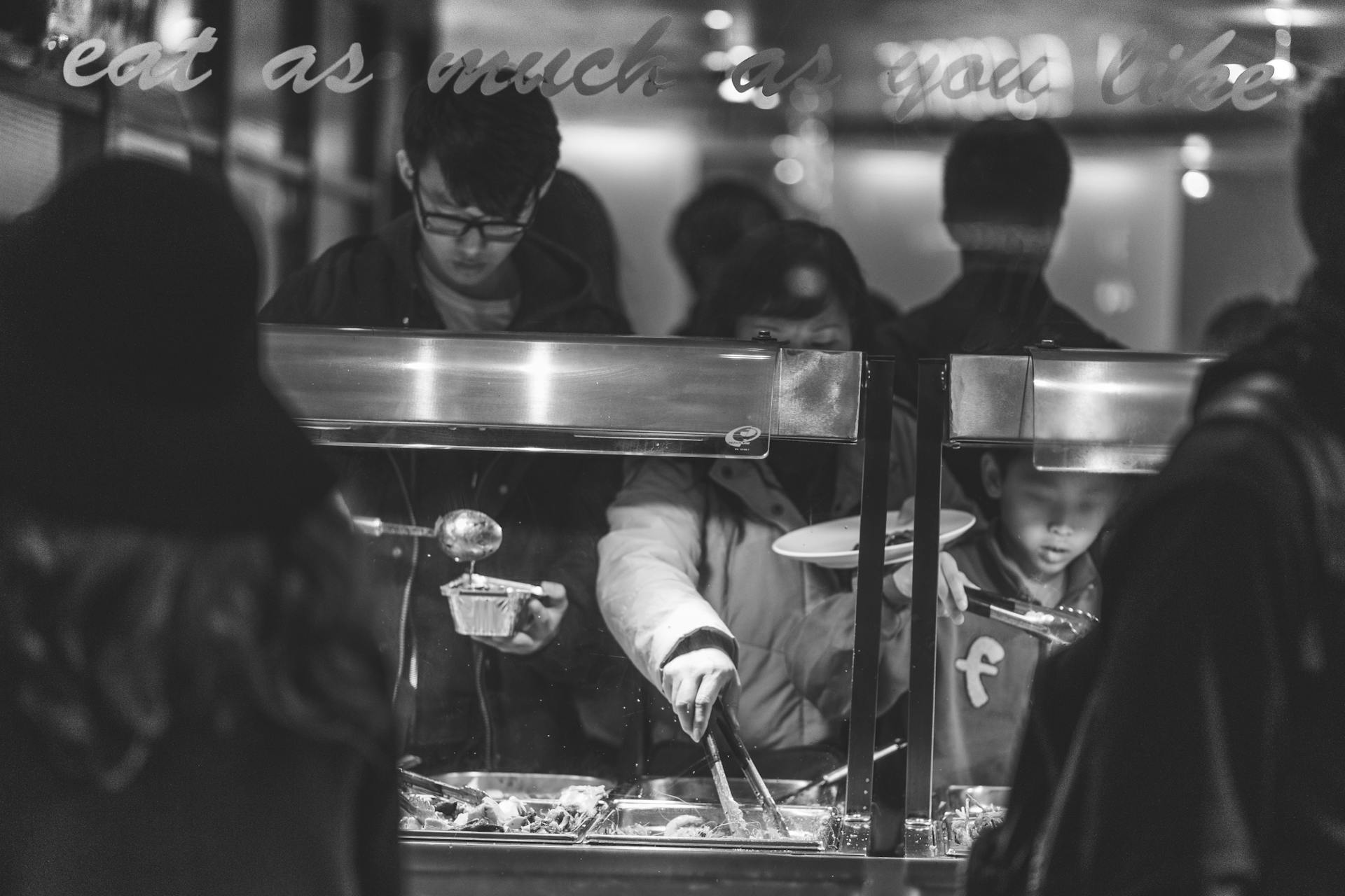 A candid black and white photo of people serving themselves at a buffet