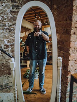 A man captures a selfie in a mirror, set in a modern loft with exposed brick walls.