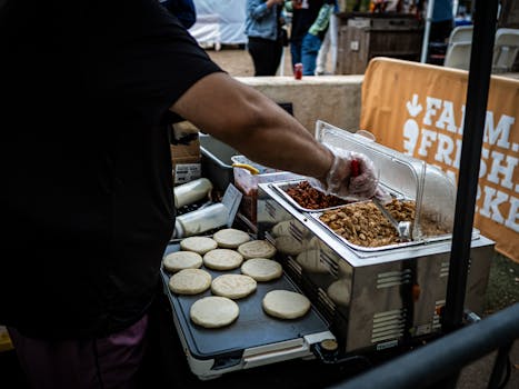 Street vendor prepares arepas with toppings at an outdoor market food stall.