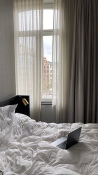 A cozy bedroom setting with a laptop on a bed, featuring a window view of Belgian architecture.