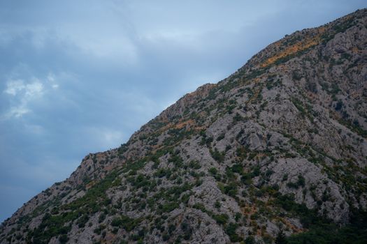A scenic view of a rocky mountain with dense vegetation under a cloudy sky.