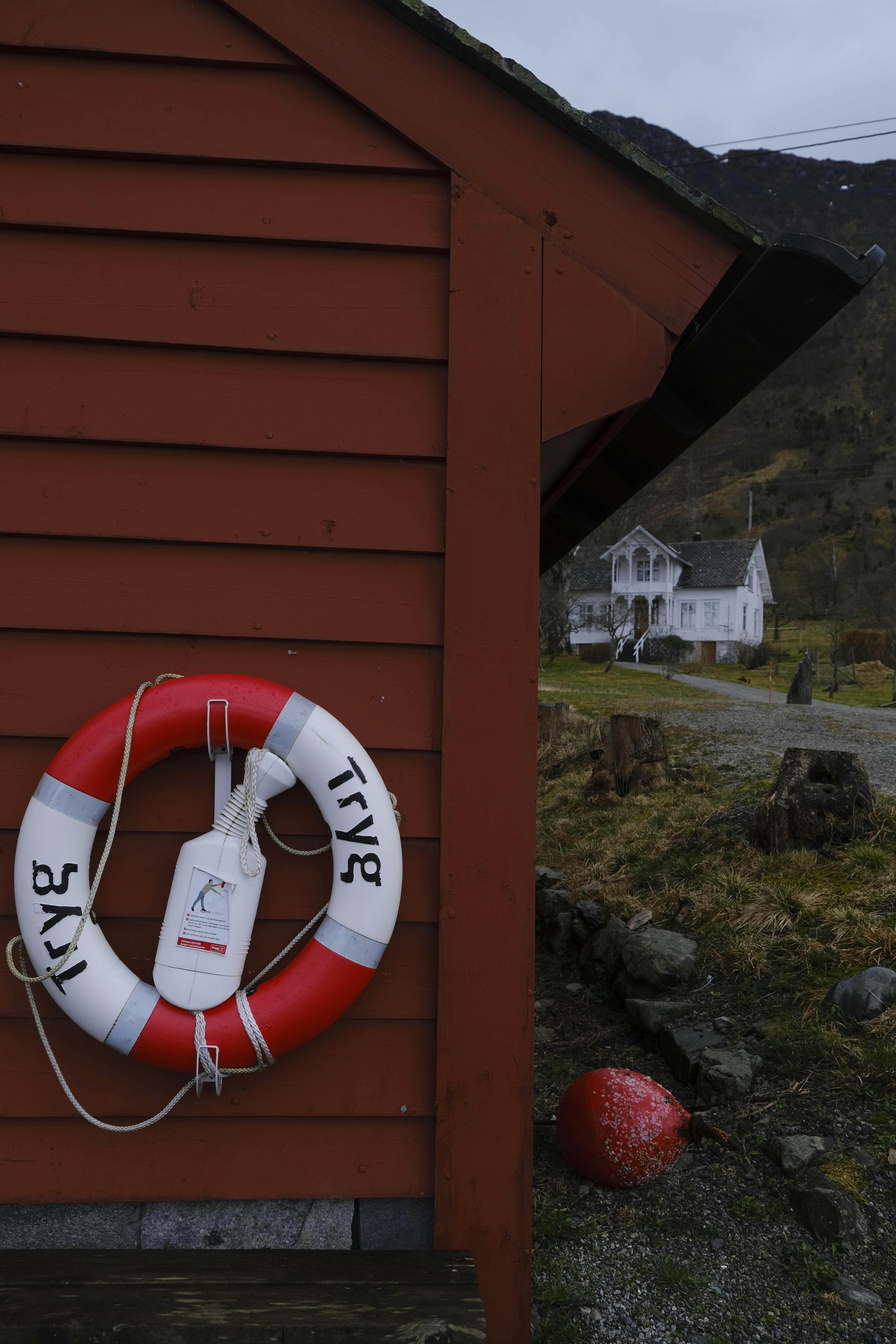 Red shed with lifebuoy by a seaside cottage in a rural landscape.