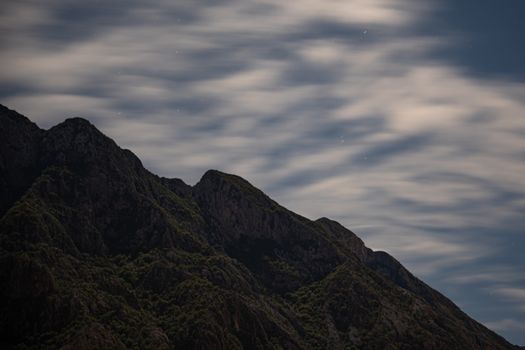 Peaceful mountain scene with scenic clouds and stars at night.