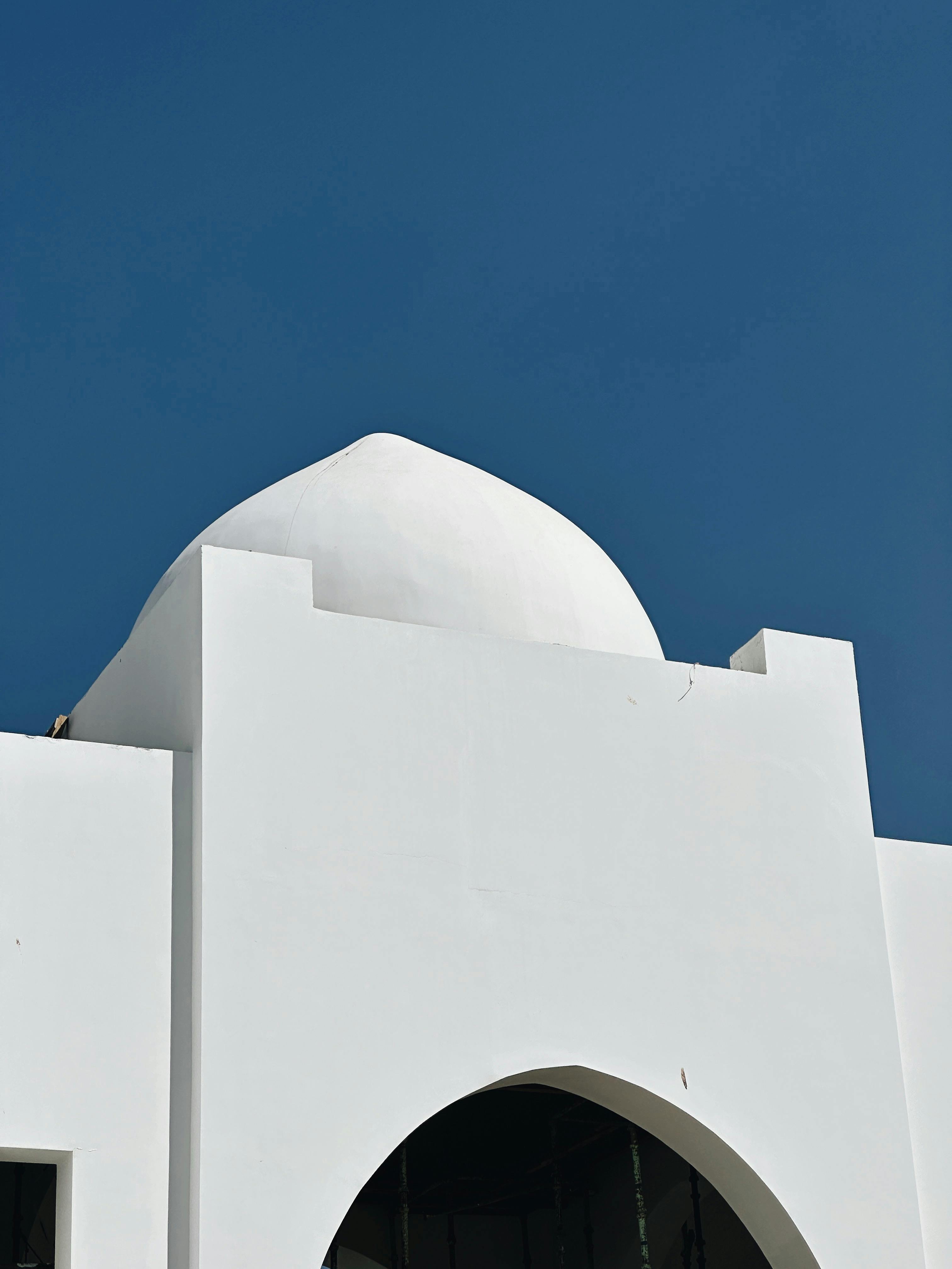 grátis Uma deslumbrante cúpula branca com arco contrastando com um céu azul vibrante, perfeita para temas de viagens ou arquitetura. Foto profissional