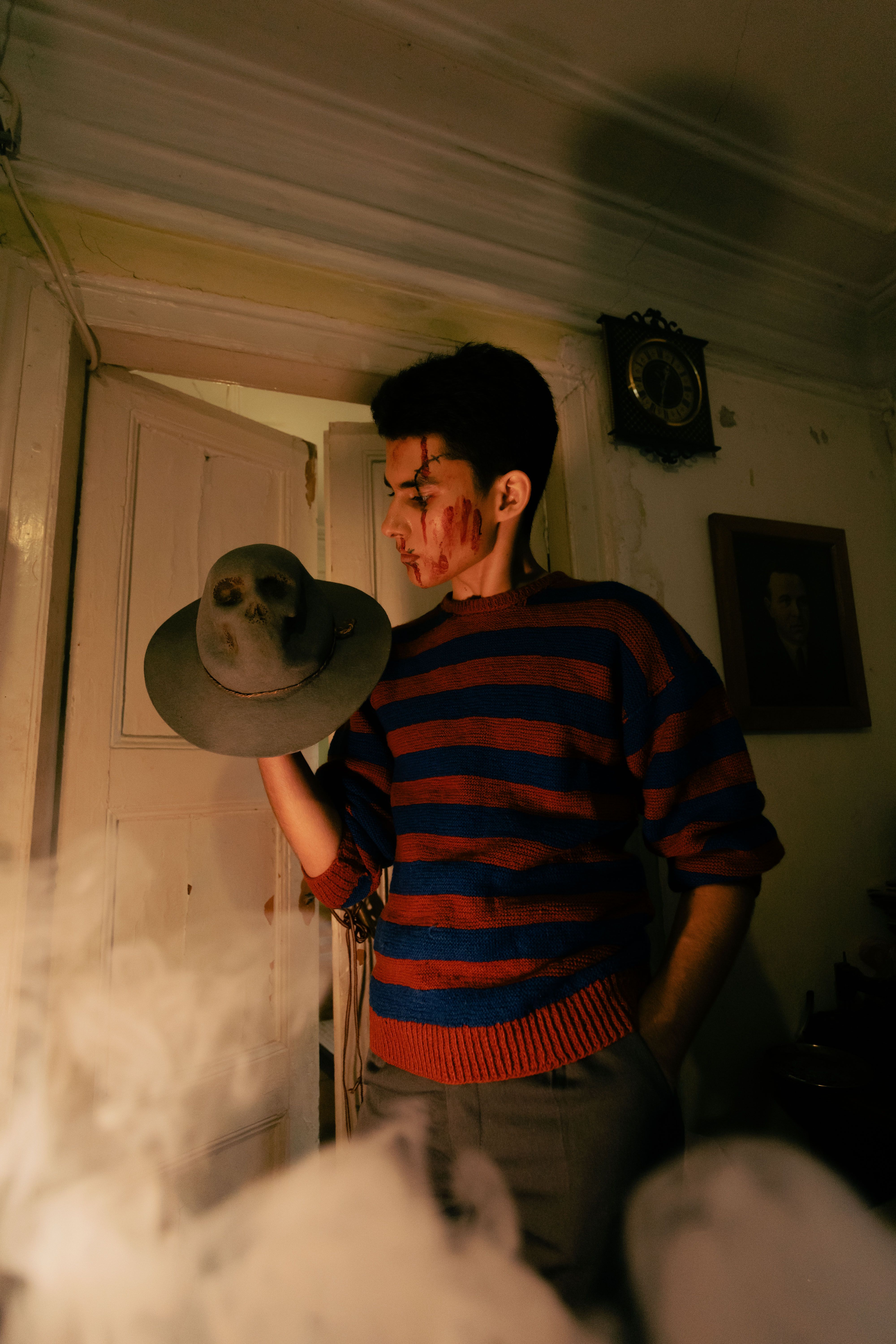 A dramatic portrait of a man holding a skull-adorned hat, indoors with atmospheric lighting.