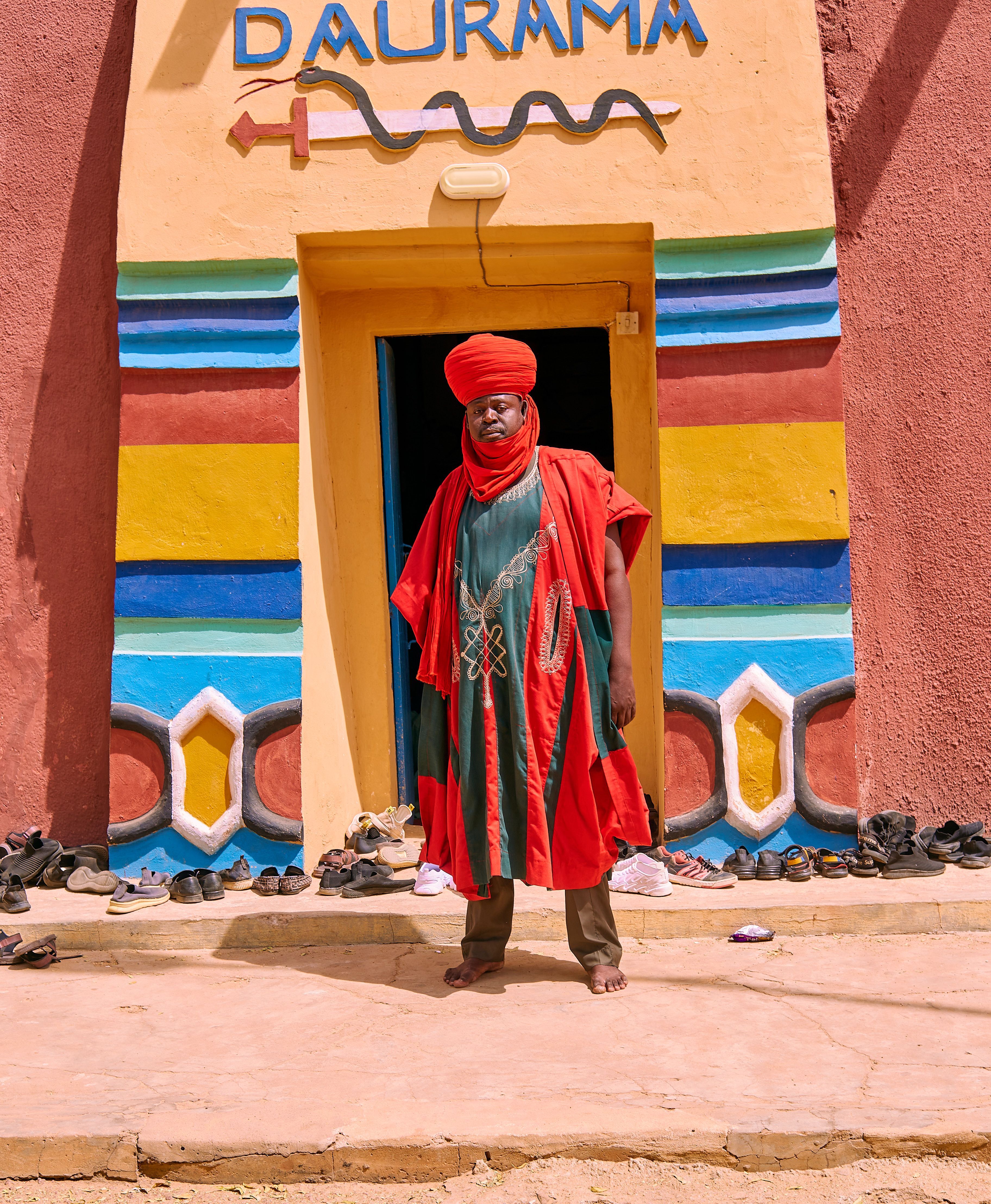 A person in traditional clothing stands by a vibrant doorway of a building labeled 'Daurama'.