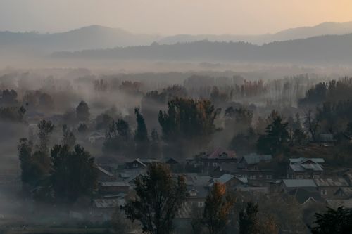 Free A serene, mist-filled morning scene in Srinagar with village rooftops and distant mountains. Stock Photo