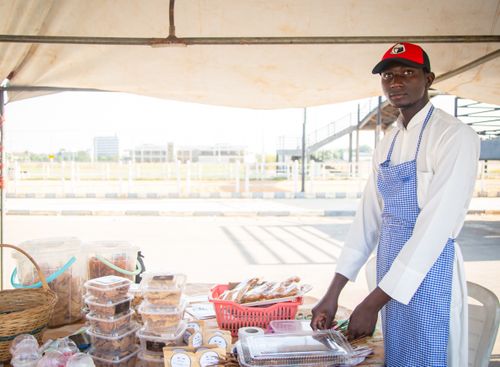 Free A young male vendor in Kaduna, Nigeria, selling baked goods at an outdoor market stall. Stock Photo