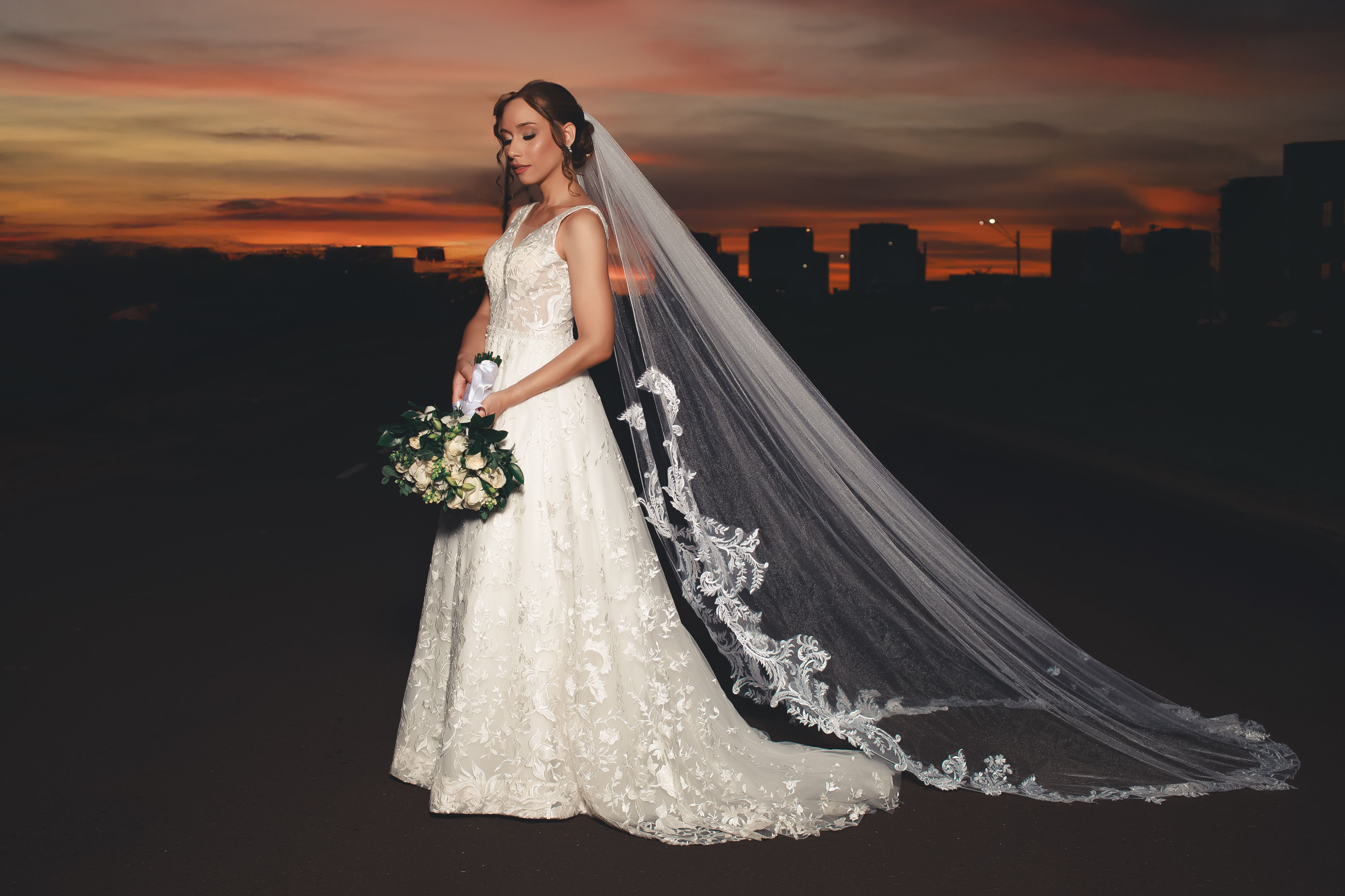 Stunning bride in lace gown with veil during a vibrant sunset.