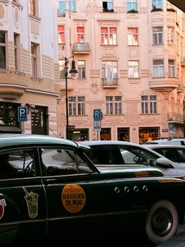 A vintage car parked in front of classic European architecture during sunset.