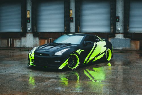 Free A stylish sports car with neon green accents parked in an industrial setting on a rainy day. Stock Photo