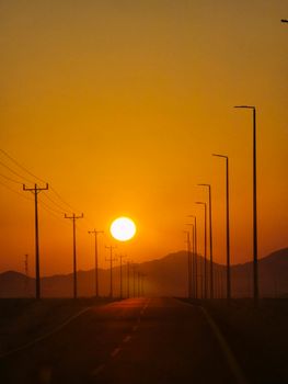 Captivating sunset view on a road lined with electric poles and mountain silhouettes.