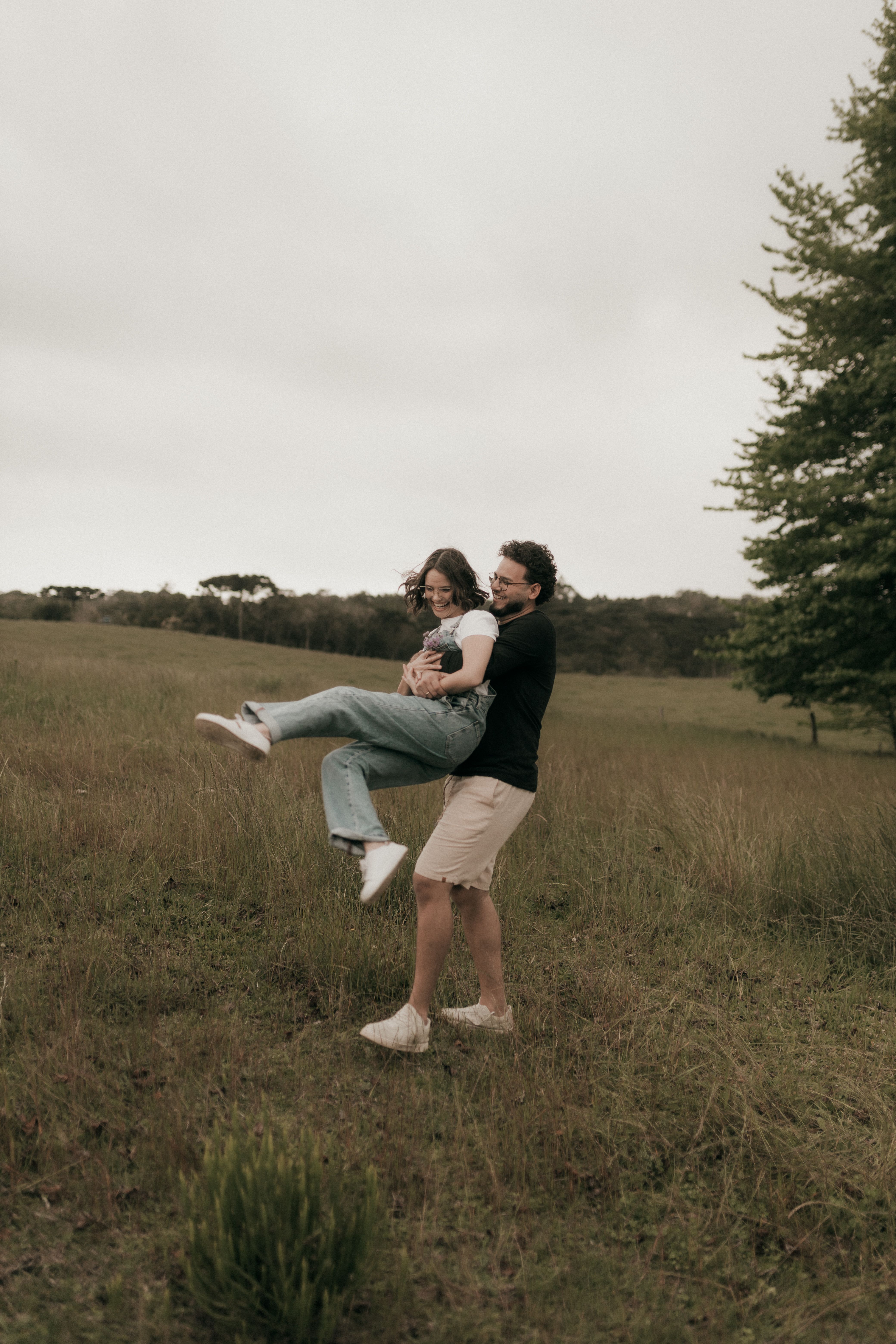 A joyful couple playing in an open field on a cloudy day, embracing happiness and nature.