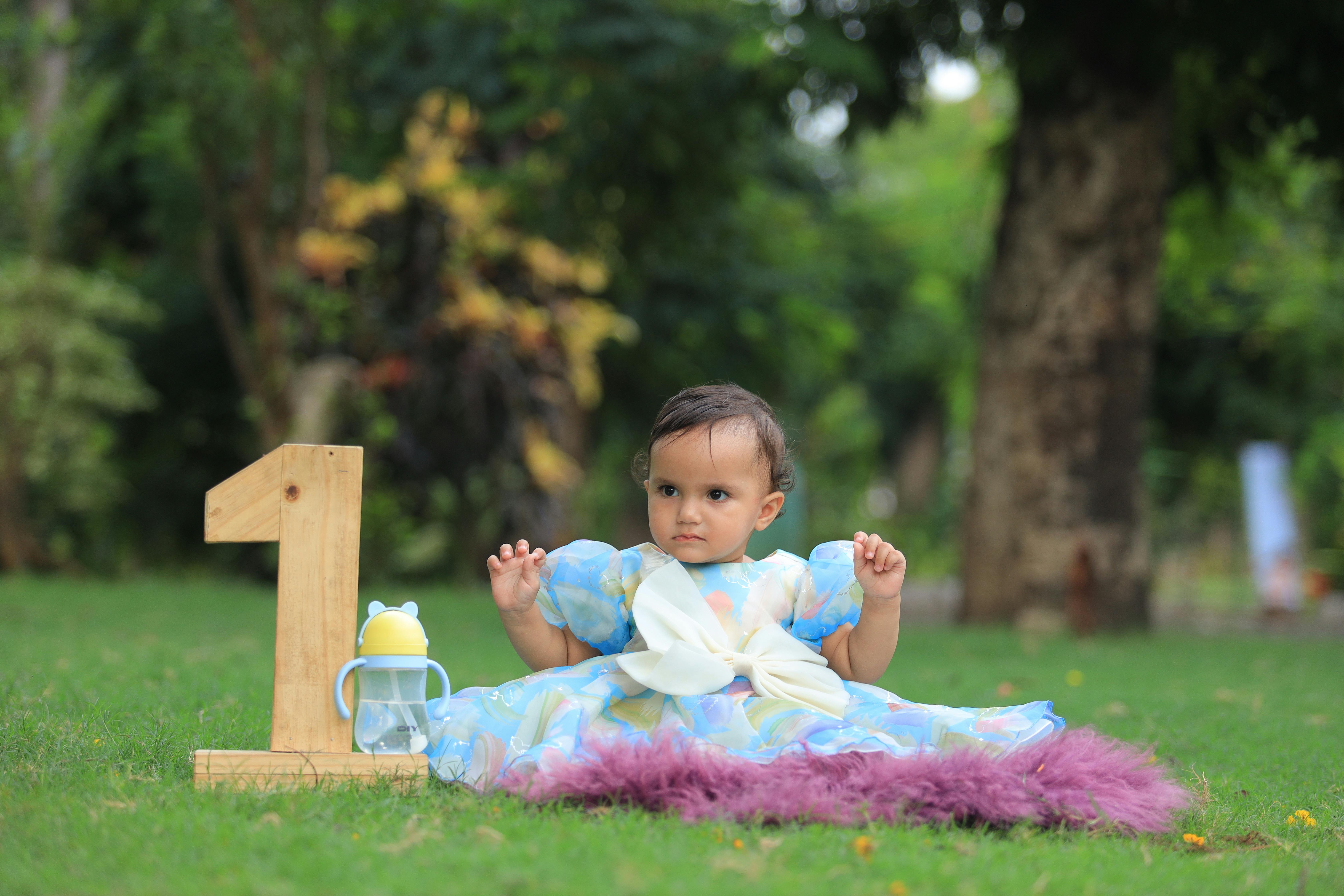 A cute baby in a dress celebrates her first birthday outdoors with a wooden number one.