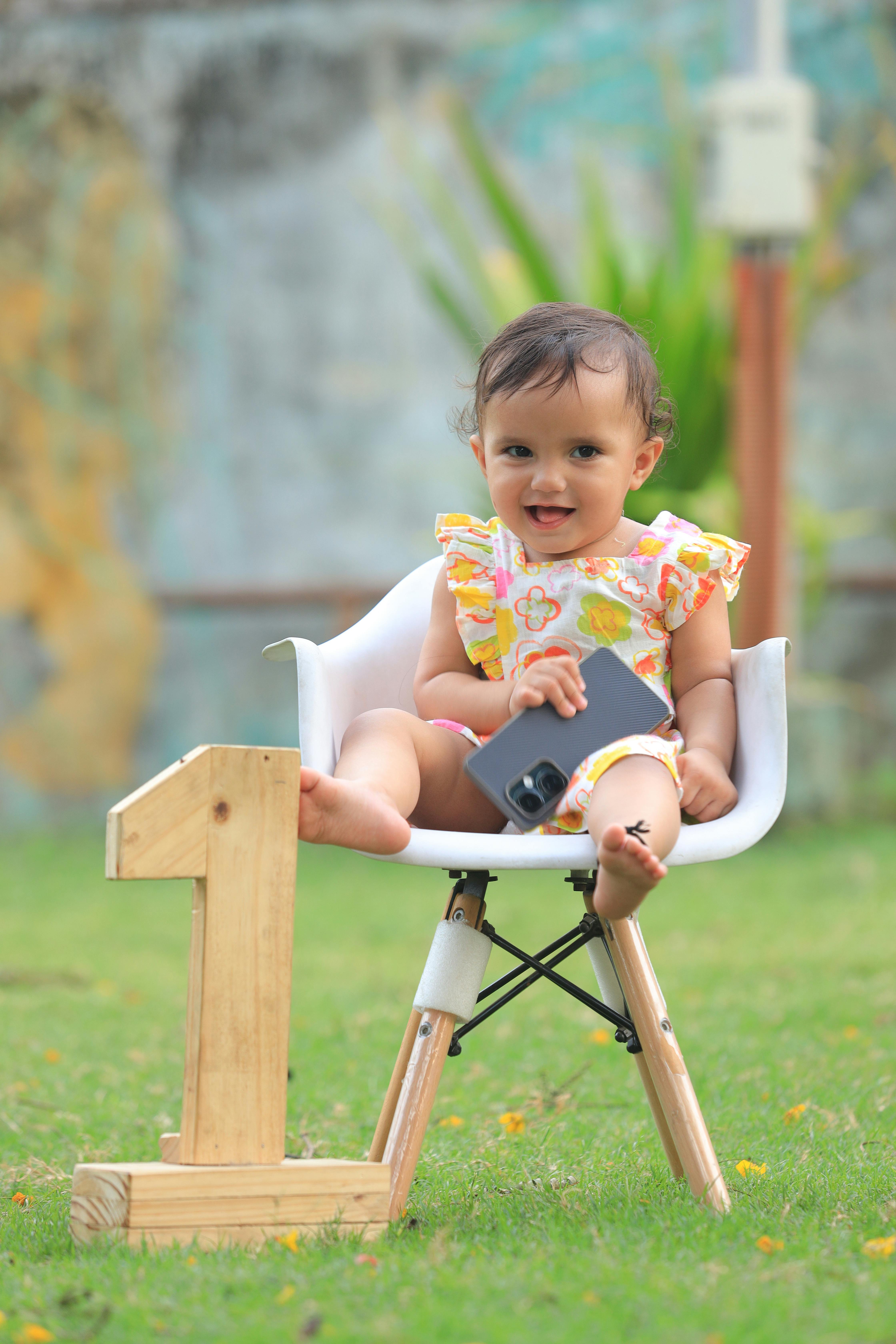 A cute baby celebrates their first birthday outdoors with a wooden number one decoration.