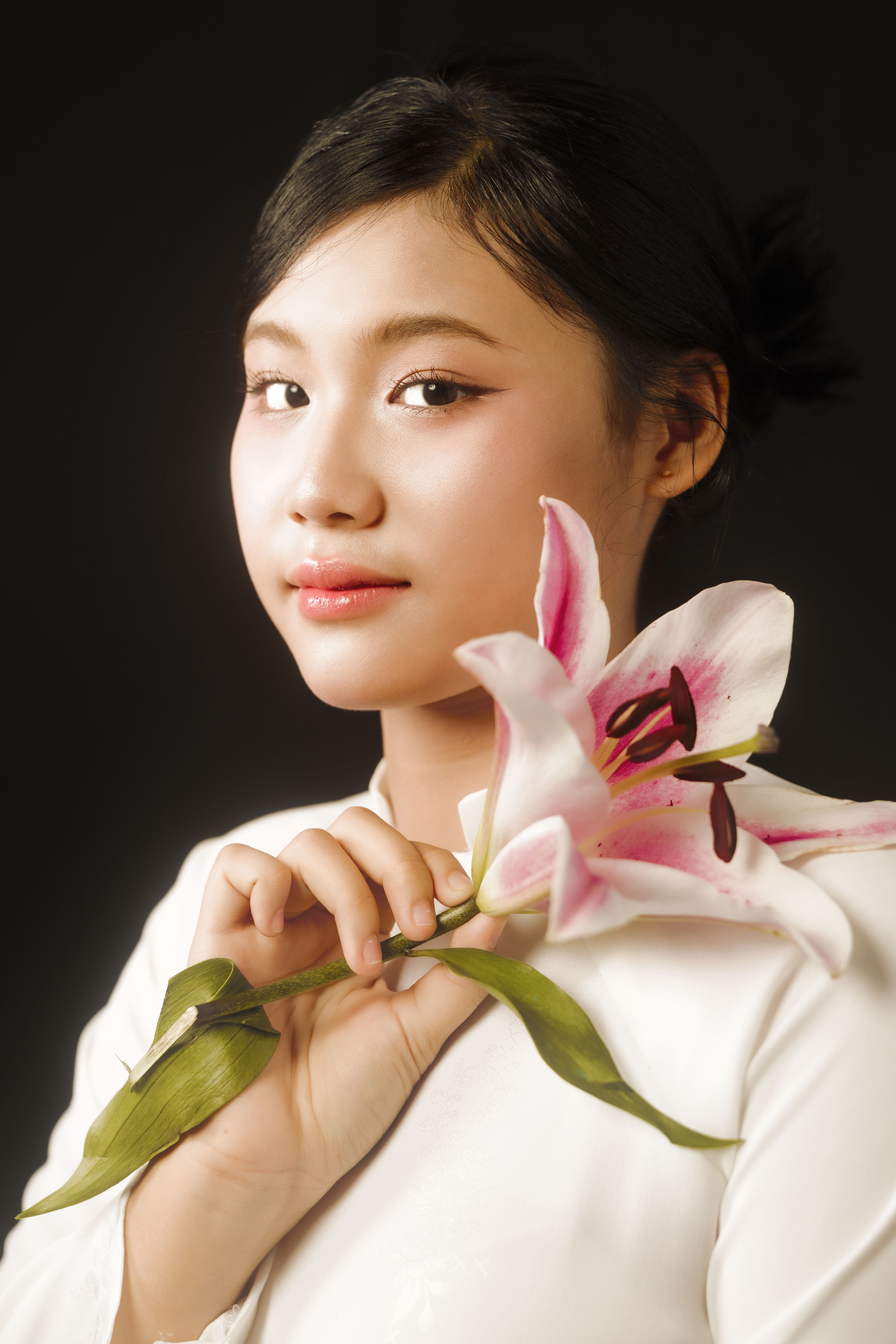 A serene portrait of a young woman holding a pink lily against a dark background.