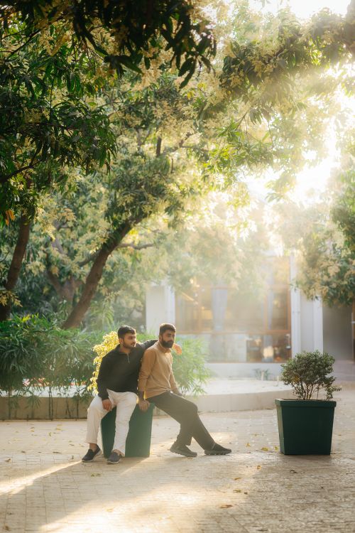 Free Two men casually sitting in a sunlit outdoor garden with lush greenery. Stock Photo