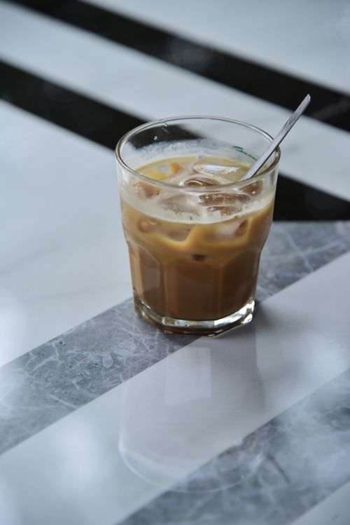 Free Glass of iced coffee with a spoon on a sleek marble table with reflections. Stock Photo