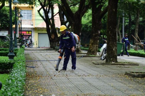 Free A city worker wearing protective gear uses a leaf blower to clean a public park pathway. Stock Photo