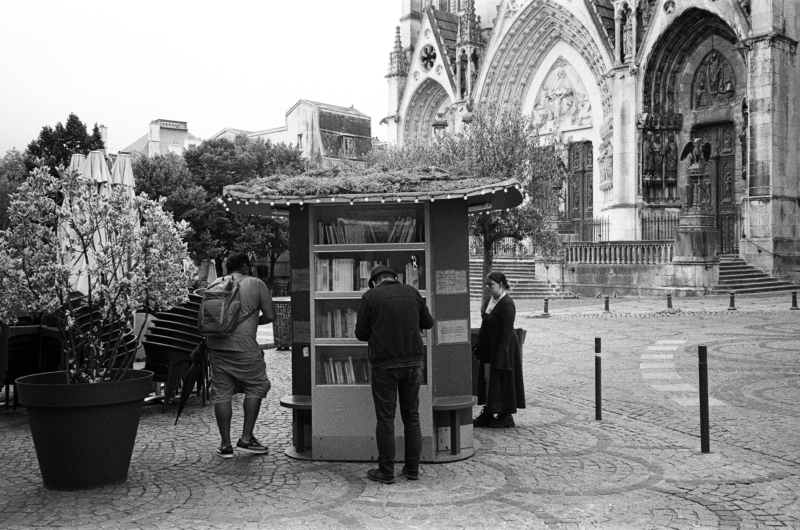 Black and white photo of people at a street library near a Gothic cathedral in Nancy, France.