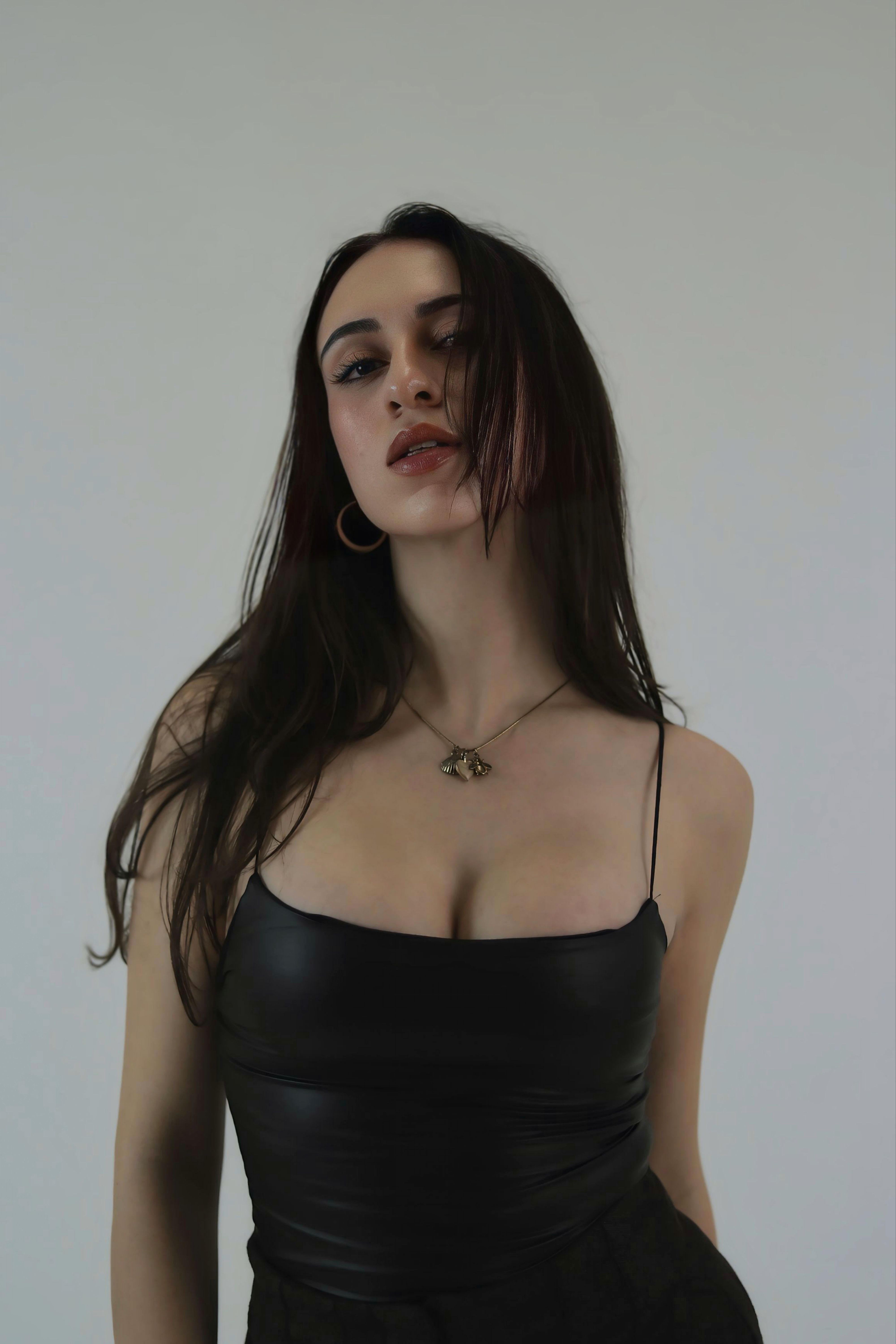 Confident woman in a black leather dress posing against a simple background.