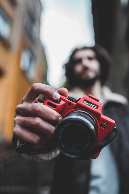 Shallow Focus Photography of Man Holding Red Sony Camera