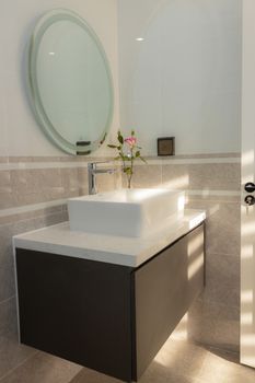 A modern bathroom with minimalist vanity and round mirror, sunlit.