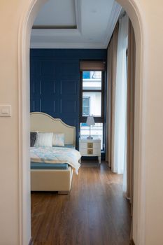 Elegant bedroom with blue accent wall and wooden flooring, viewed through a white archway.